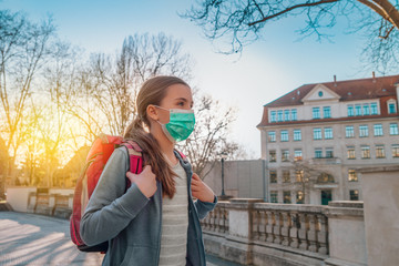 a school-aged girl walking outside with her backpack on and a surgical mask over her mouth and nose