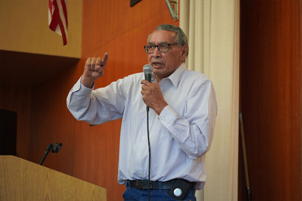 an image of an older man holding a microphone and speaking to an audience