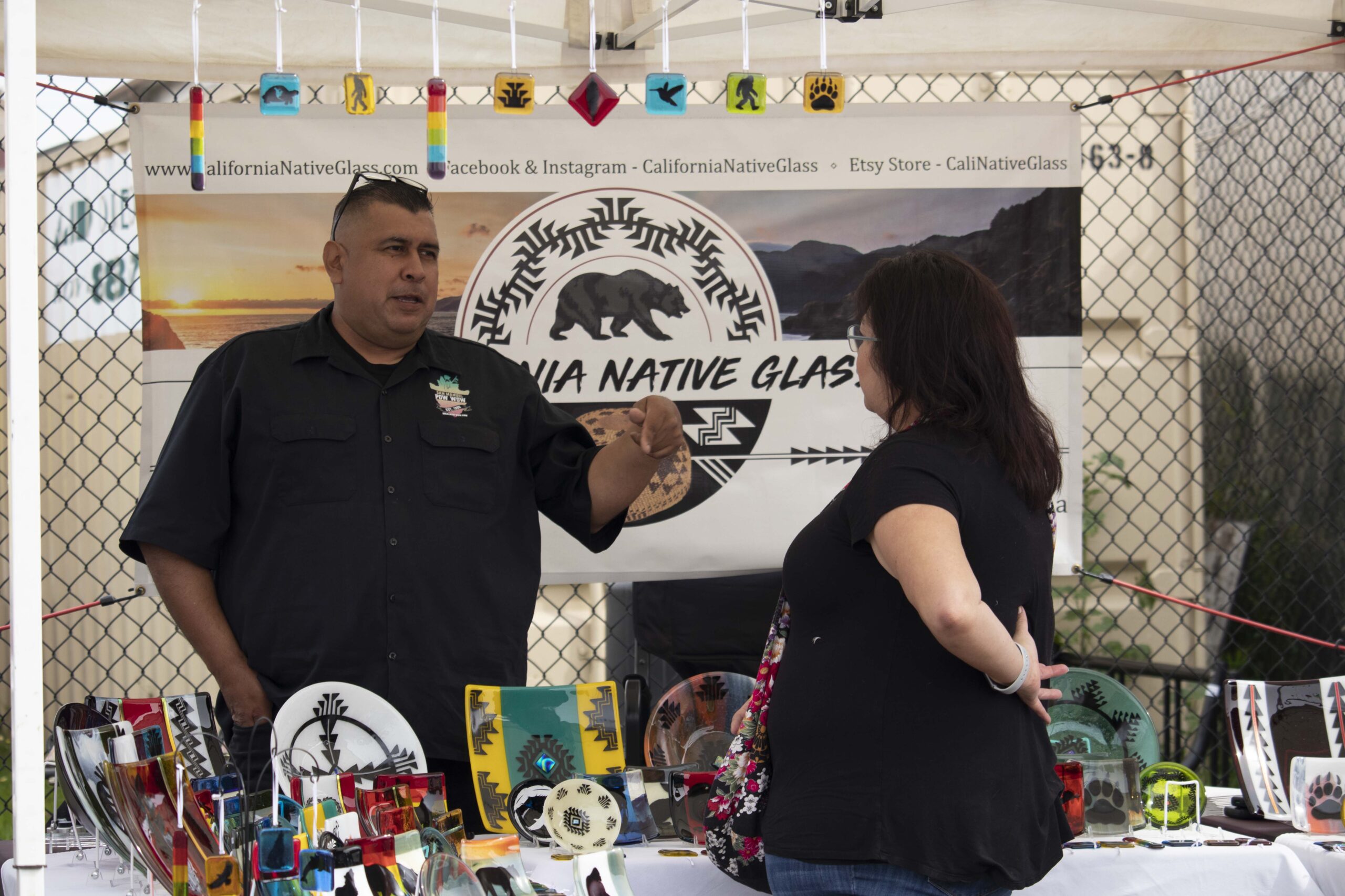 Indigenous Red Market vendor displaying traditional Native American art and talking with an attendee